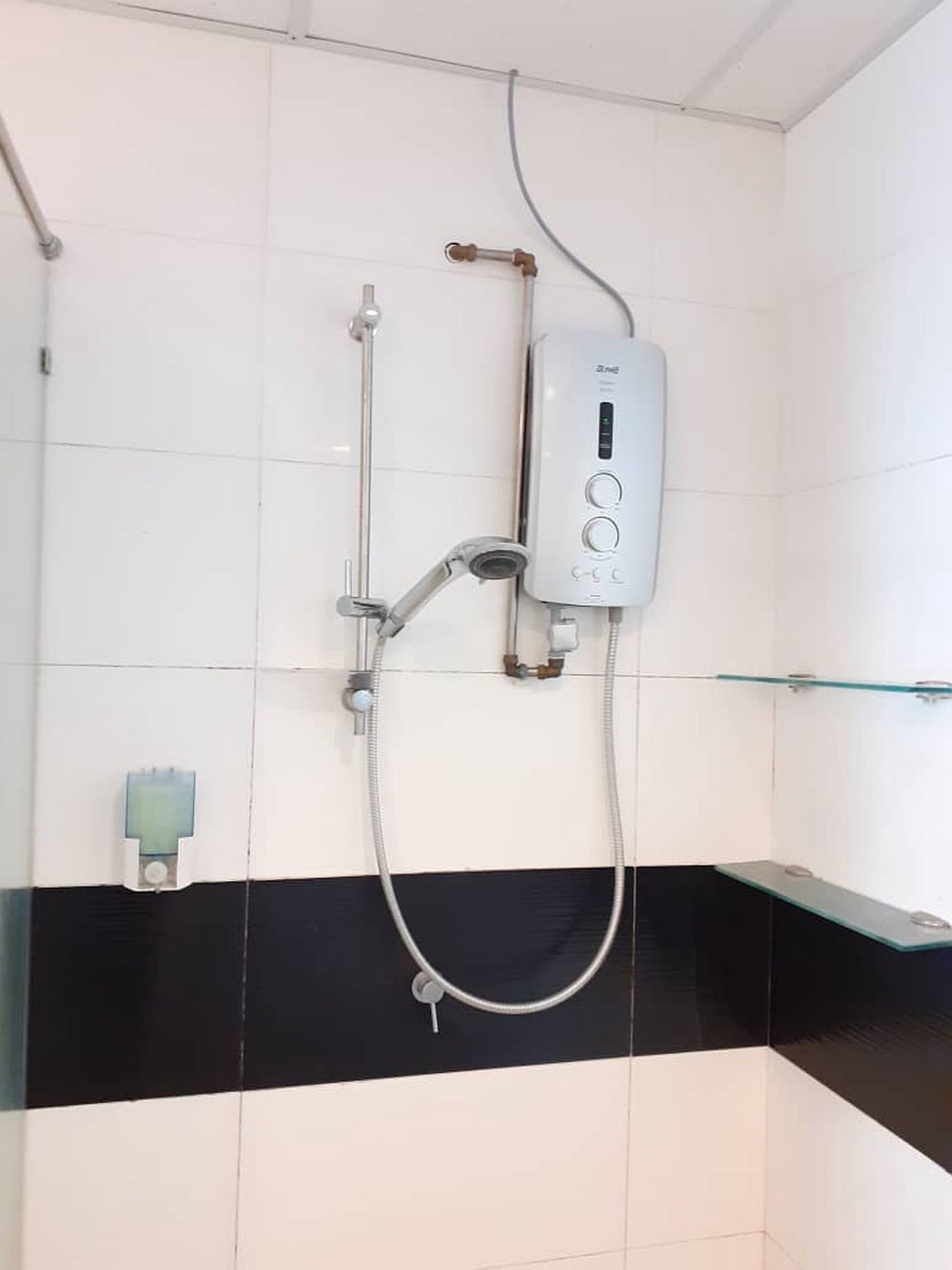 A clean tiled en-suite bathroom with water heater and glass shelving at Merlene Suites