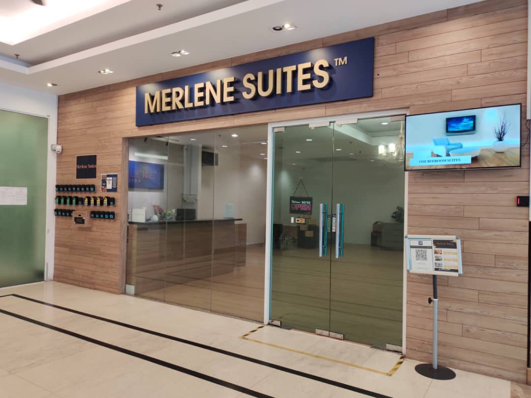 The Merlene Suites reception desk at Mansion One, with the gold-on-navy wordmark above a wood-panelled wall